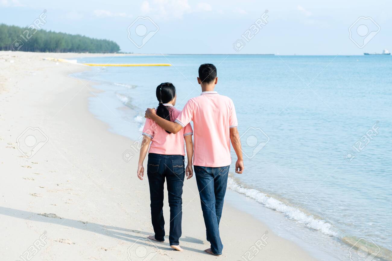 Young Couples Walk Hand In Hand On The Beach In The Summer Holidays