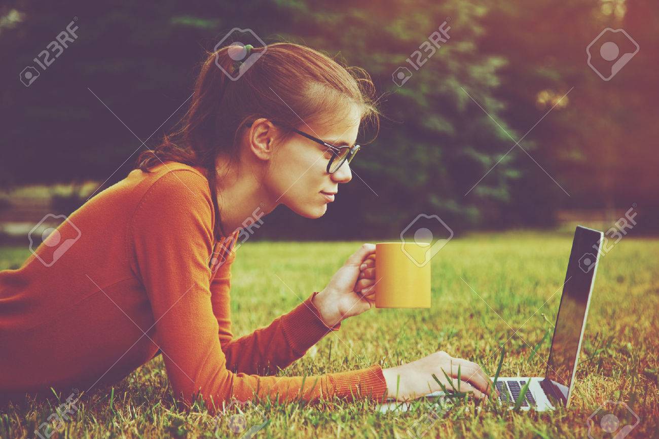 girl lying on the grass and using laptop and typing with coffee or tea mug - 46616741 girl lying on the grass and using laptop and typing with coffee or tea mug - 46616741