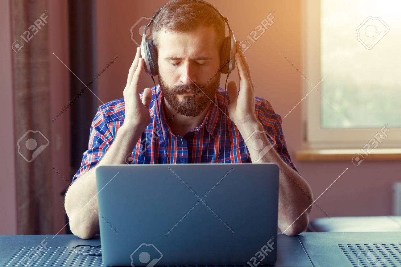 ノート パソコンで音楽を聴くヘッドフォンでハンサムなひげを生やした男 の写真素材 画像素材 Image