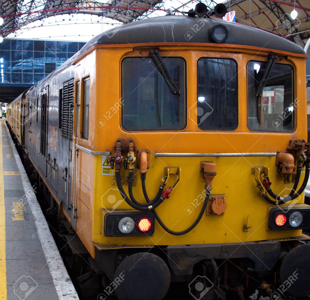 オレンジ色の近代的な貨物列車は いくつかの汚れやすす および部分的に背景に英国の旗で ロンドンの鉄道駅に駐車しました の写真素材 画像素材 Image