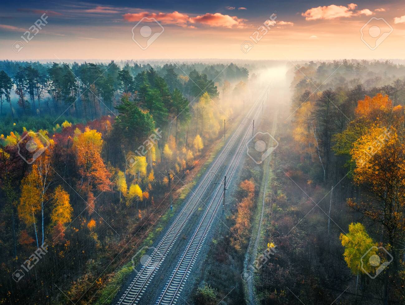 Vue aérienne du magnifique chemin de fer dans la forêt d'automne au lever du soleil brumeux. paysage industriel avec gare, ciel bleu avec nuages, arbres à feuilles orange, brouillard. vue de dessus du chemin de fer rural à l'automne - 155421474 Vue aérienne du magnifique chemin de fer dans la forêt d'automne au lever du soleil brumeux. paysage industriel avec gare, ciel bleu avec nuages, arbres à feuilles orange, brouillard. vue de dessus du chemin de fer rural à l'automne - 155421474