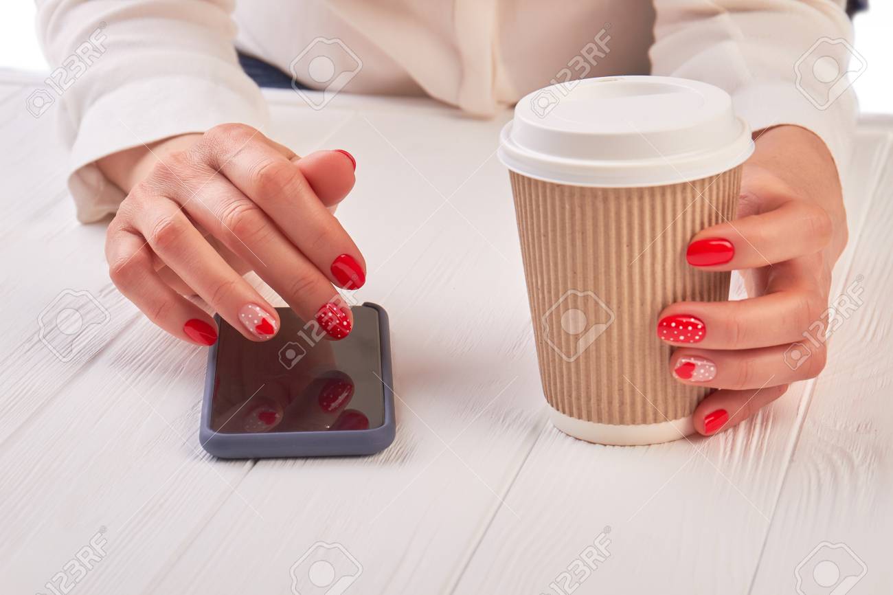 スマートフォンを使ったコーヒーの女性 女性は コーヒーの使い捨てのカップを保持し タッチスクリーンの携帯電話 白い木製のテーブルを使用して手を手入れしました の写真素材 画像素材 Image