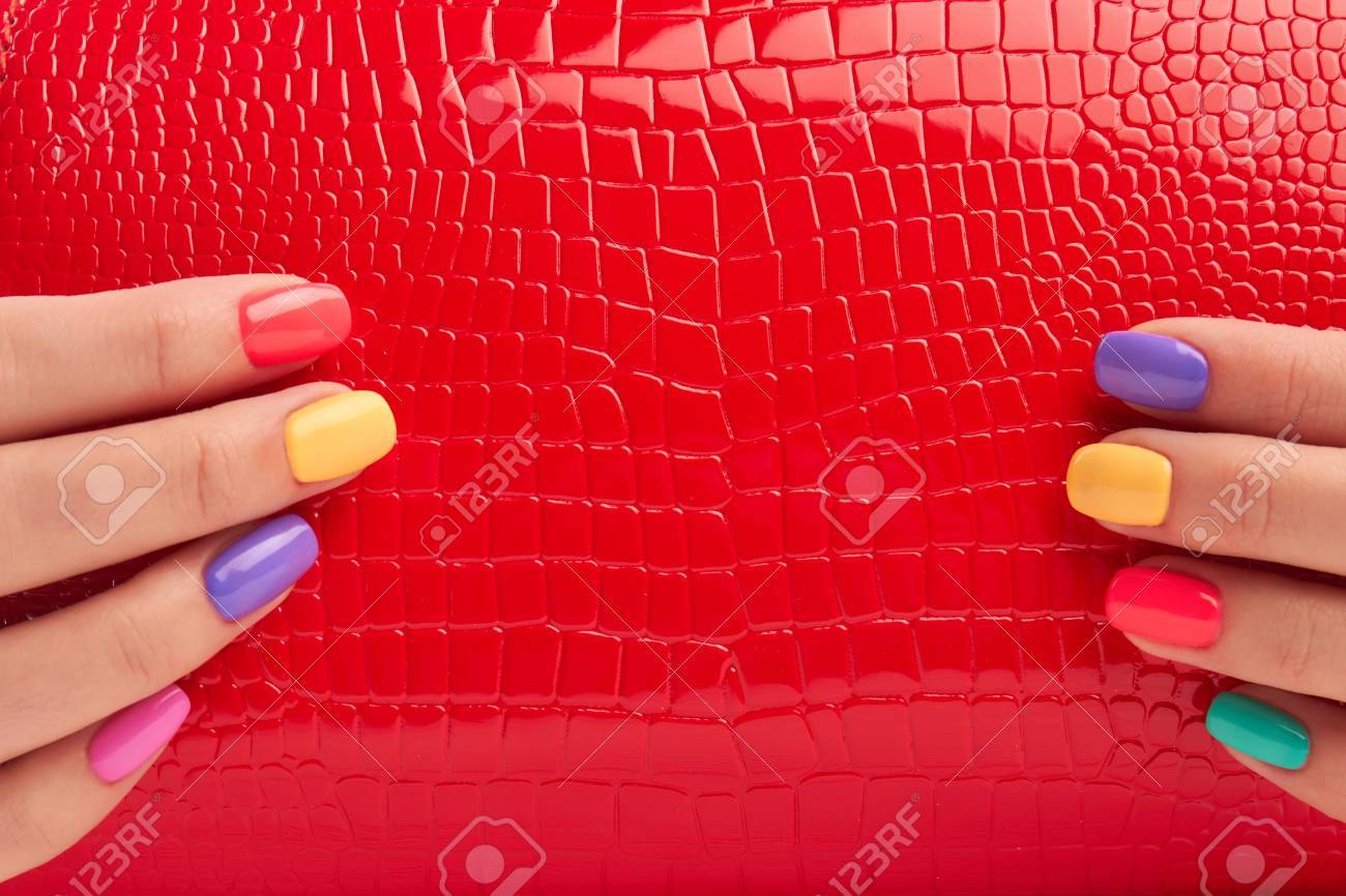 手入れの行き届いた手の赤いバッグを閉じます 色とりどりのマニキュアで女性の手に赤い漆塗りのハンドバッグの詳細です 女性のファッション小物 の写真素材 画像素材 Image