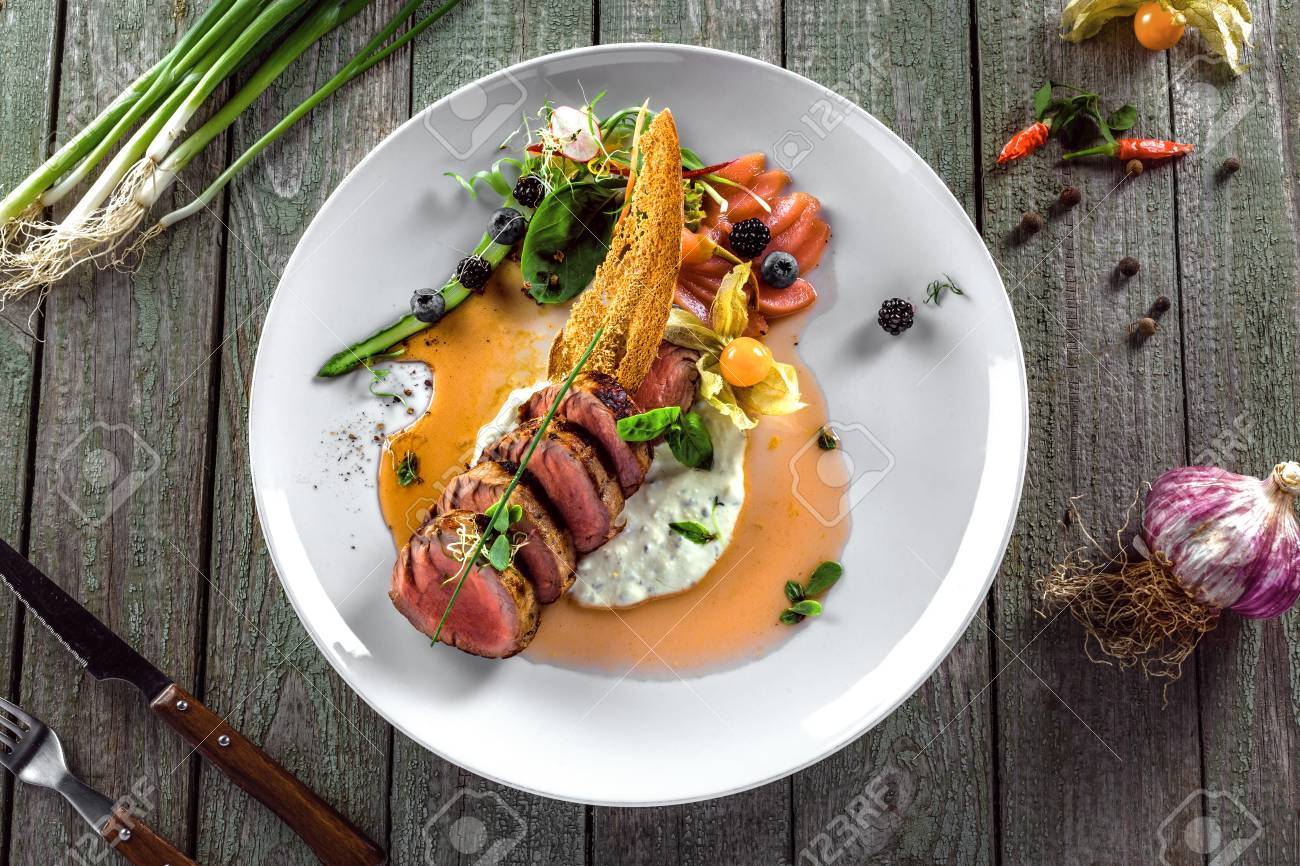 おいしい中珍しい肉ステーキ ソースと皿にサラダ 健康食品は肉の切り身と木製のテーブルに新鮮なハーブから成っています 平面図です の写真素材 画像素材 Image