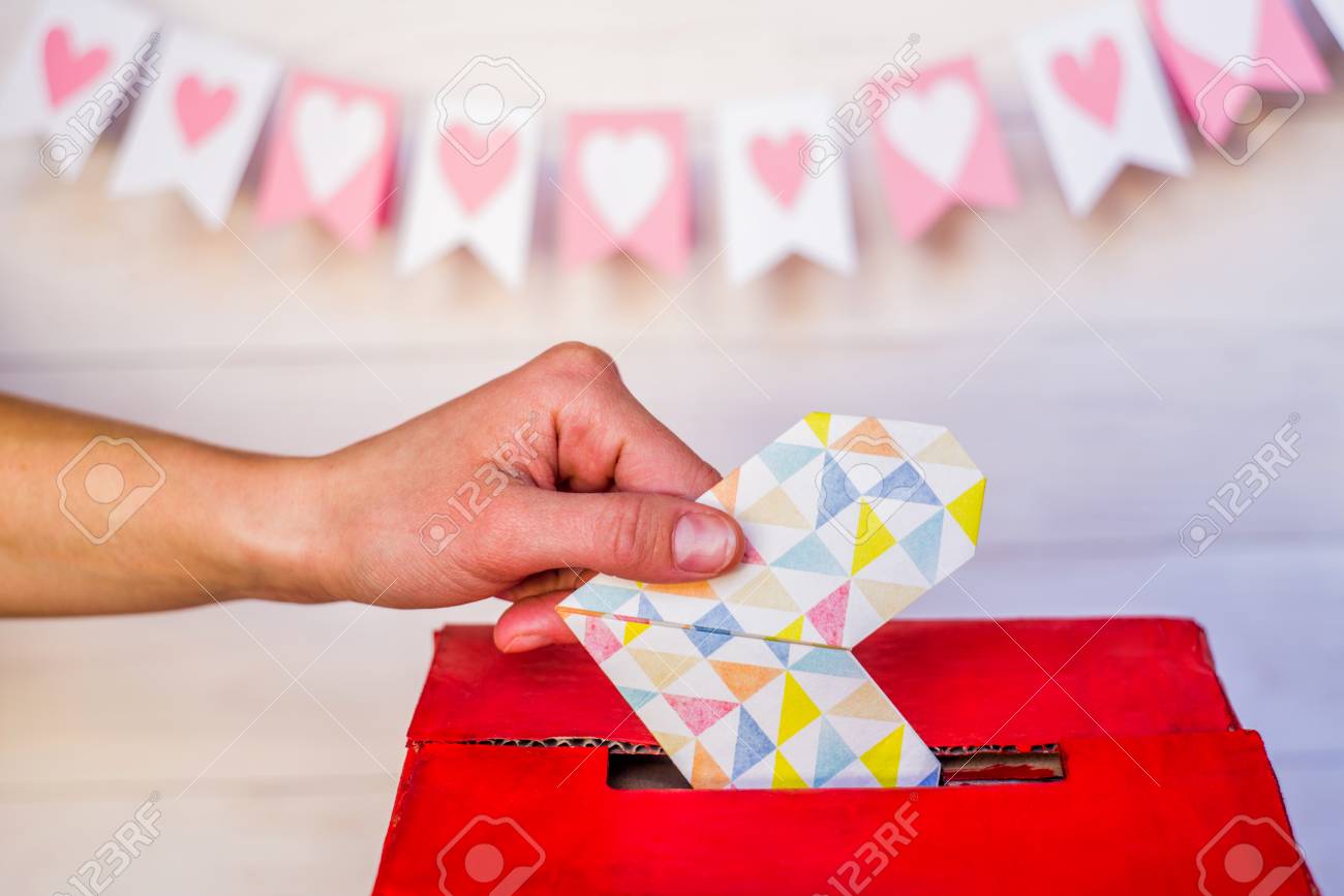 バレンタインデーのコンセプト 箱に折り紙の心を置く女性の手 白い木製の背景にロープにぶら下がっている白とピンクの旗 の写真素材 画像素材 Image