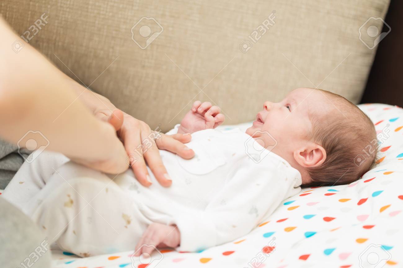 生まれたばかりの赤ちゃんは疝痛 と 彼女の背中に白敷設に身を包んだ彼女のおなかの上母の手 の写真素材 画像素材 Image
