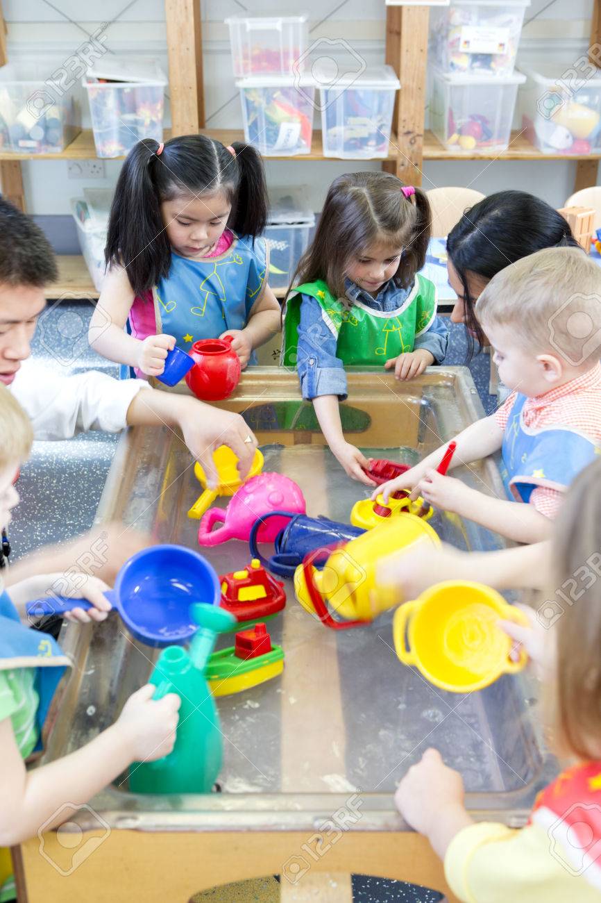 Group of nursery children playing at a water table with their teacher. - 60256175 Group of nursery children playing at a water table with their teacher. - 60256175