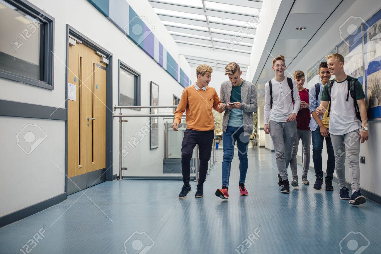 Group of teenage boys are walking down the school hall together to go for their lunch break. They are talking and laughing and some of the boys are using smart phones. - 72952760 Group of teenage boys are walking down the school hall together to go for their lunch break. They are talking and laughing and some of the boys are using smart phones. - 72952760