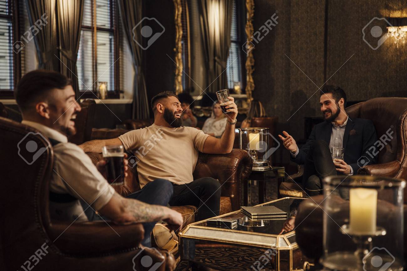 Three men are enjoying drinks in a bar lounge. They are talking and laughing while drinking pints of beer. - 74055608 Three men are enjoying drinks in a bar lounge. They are talking and laughing while drinking pints of beer. - 74055608