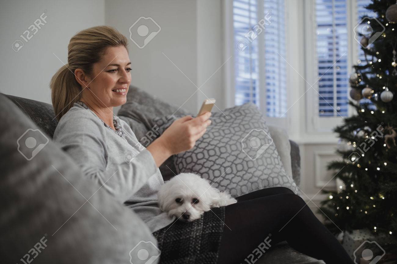 成熟した女性は クリスマス時に彼女の家のリビング ルームでリラックス 彼女の犬は彼女の膝に座っていると 彼女はスマート フォンを使用しています の写真素材 画像素材 Image 0507 成熟した女性は クリスマス時に彼女の家のリビング ルームでリラックス 彼女の犬は彼女の膝に座っていると 彼女はスマート フォンを使用しています の写真素材 画像素材 Image 0507