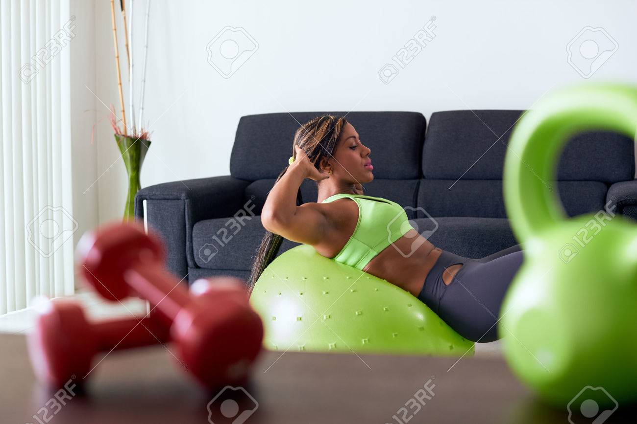 Young adult african american woman in sports clothing at home, doing domestic fitness and training abdominals on swiss ball in living room - 44251261 Young adult african american woman in sports clothing at home, doing domestic fitness and training abdominals on swiss ball in living room - 44251261