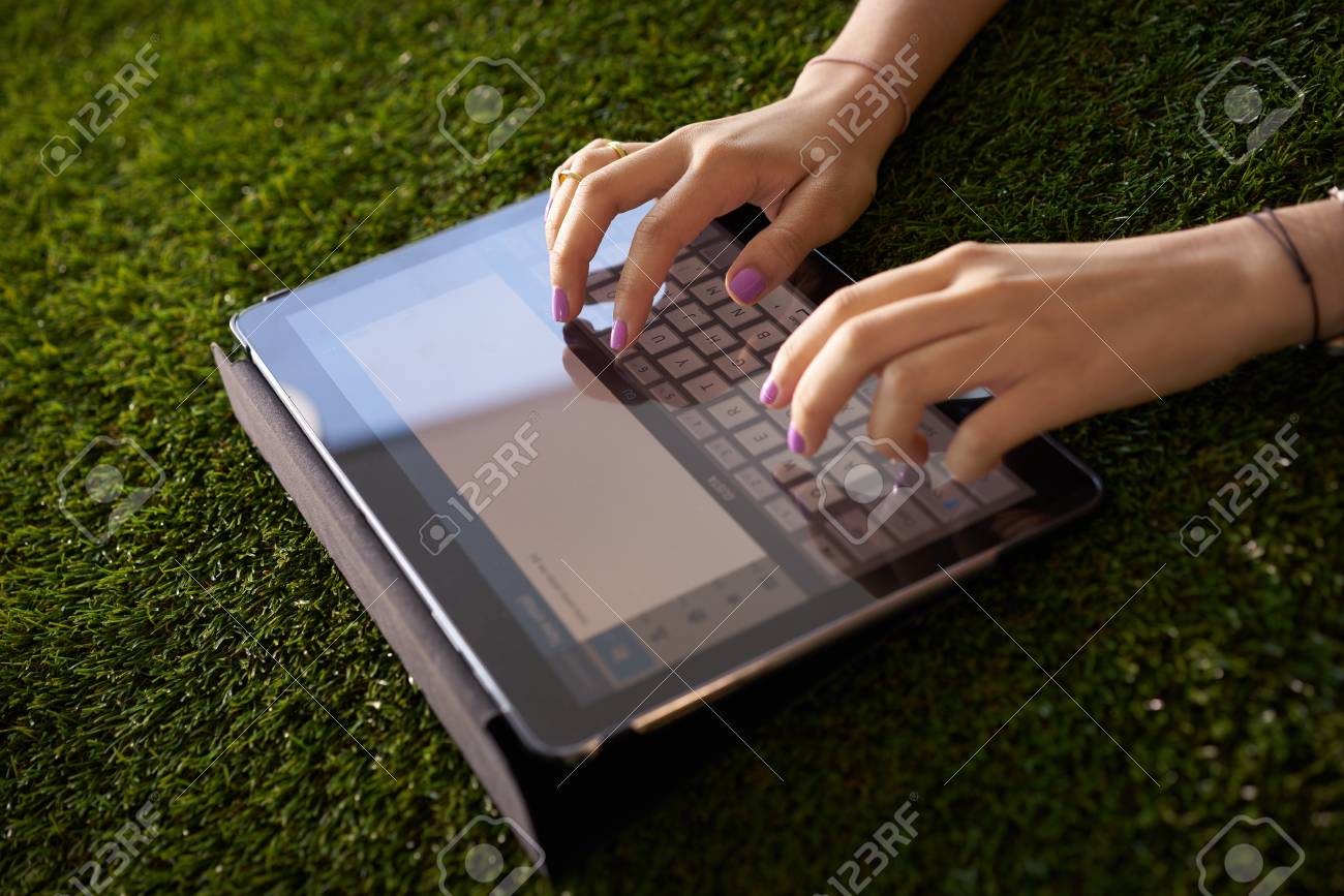 Closeup view of young woman writing on tablet pc on grass, typing an email on digital screen. - 51551644 Closeup view of young woman writing on tablet pc on grass, typing an email on digital screen. - 51551644