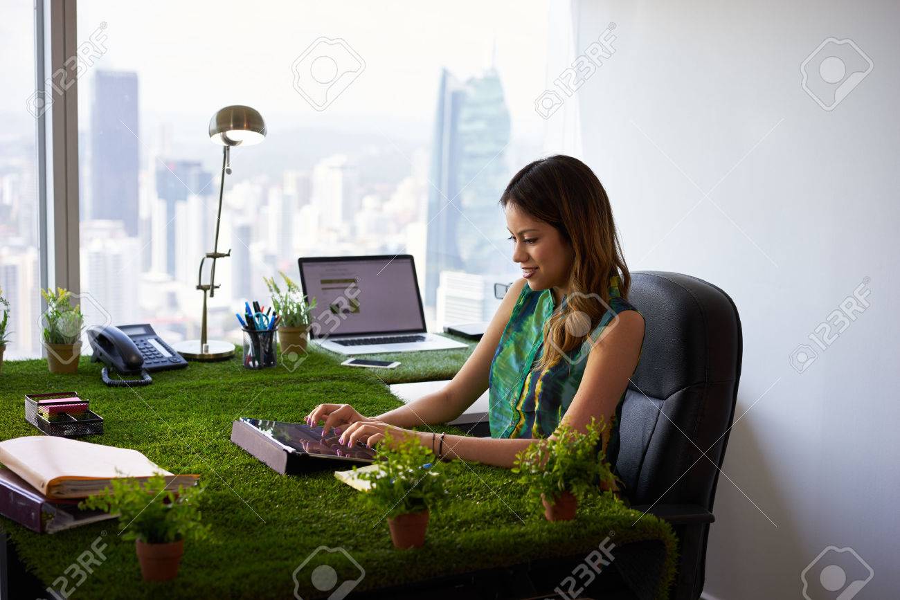 Concept of ecology and environment: Young business woman working in modern office with table covered of grass and plants. She types on tablet pc - 51551646 Concept of ecology and environment: Young business woman working in modern office with table covered of grass and plants. She types on tablet pc - 51551646