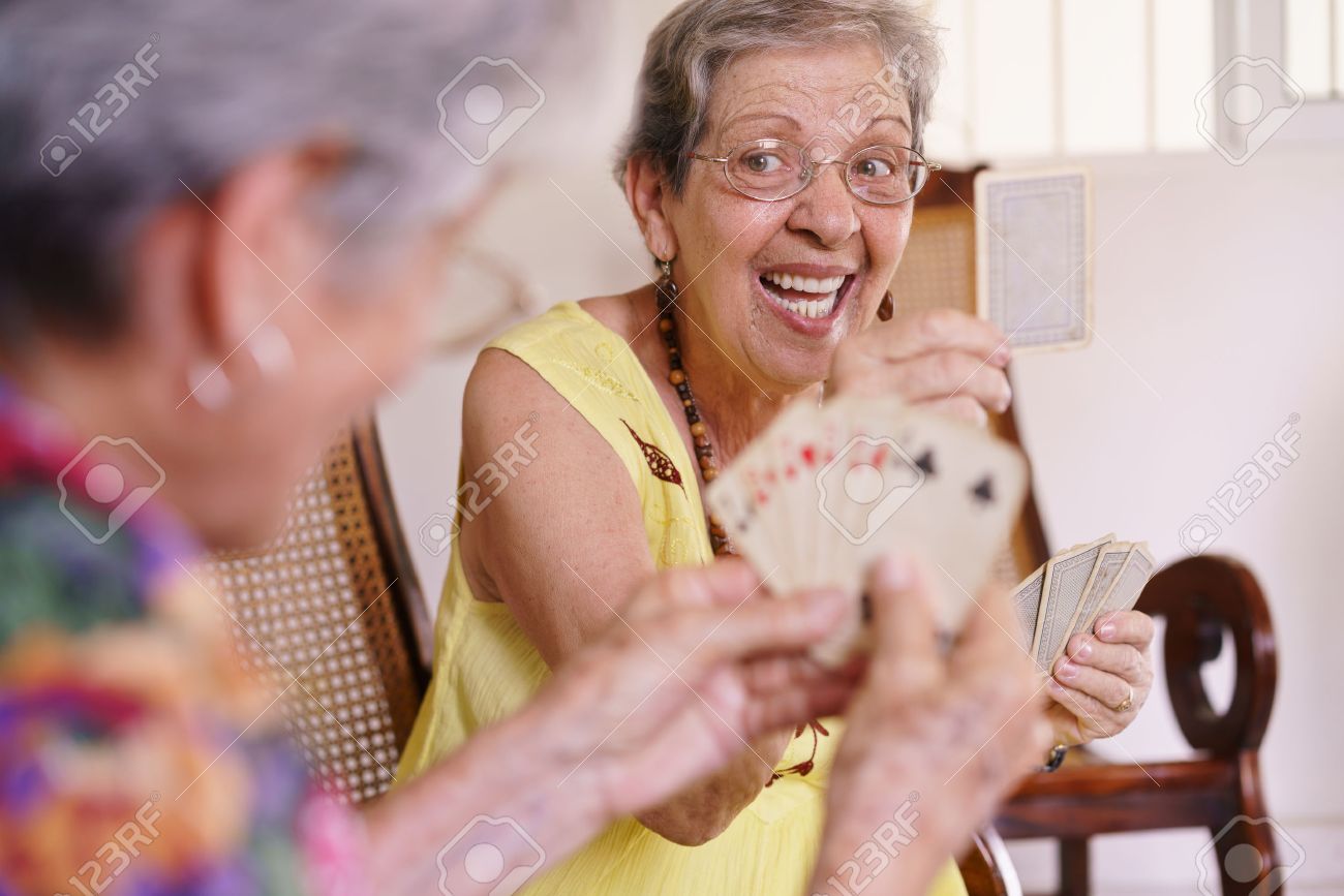 Old people in geriatric hospice: group of senior women playing cards and having fun together. An aged lady wins the game and shows a card to her rival - 56097386 Old people in geriatric hospice: group of senior women playing cards and having fun together. An aged lady wins the game and shows a card to her rival - 56097386