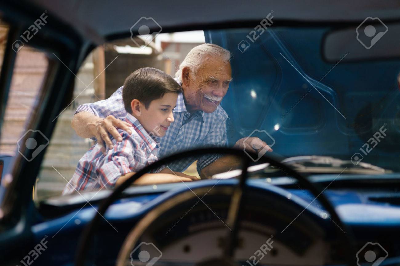Family and Generation gap. Old grandpa spending time with his grandson. The senior man shows the engine of a vintage car from the 60s to the preteen child. They smile happy. Viewed from the interior of the car - 56097407 Family and Generation gap. Old grandpa spending time with his grandson. The senior man shows the engine of a vintage car from the 60s to the preteen child. They smile happy. Viewed from the interior of the car - 56097407