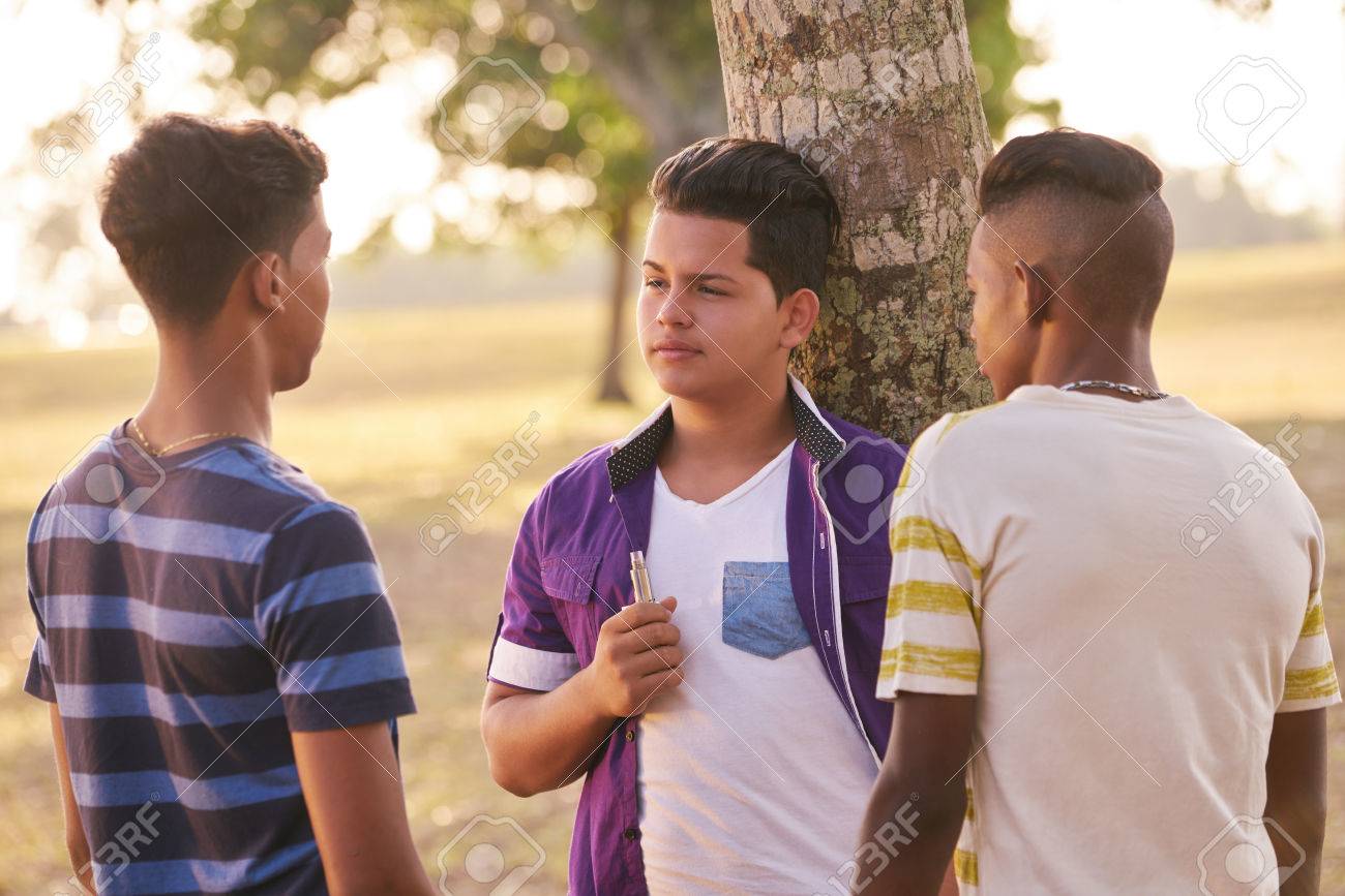 Youth culture, young people, group of male friends, multi-ethnic teens outdoors, multiracial boys together in park. Kids smoking electronic cigarette, e-cig smokers. Health problems, social issues - 58998782 Youth culture, young people, group of male friends, multi-ethnic teens outdoors, multiracial boys together in park. Kids smoking electronic cigarette, e-cig smokers. Health problems, social issues - 58998782