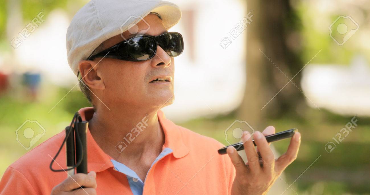 Hispanic blind man with disability. Visually impaired man using Digital Assistant and Ease of Access functions on mobile phone, voice typing to smartphone - 80274909 Hispanic blind man with disability. Visually impaired man using Digital Assistant and Ease of Access functions on mobile phone, voice typing to smartphone - 80274909