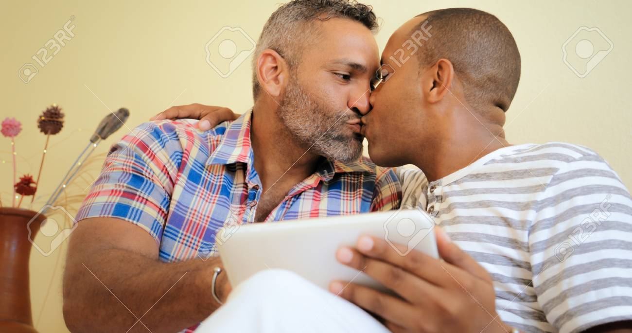 同性愛者のカップルは 自宅のタブレット Pc 上の写真を見ながらキス ヒスパニック系のゲイの男性 の写真素材 画像素材 Image