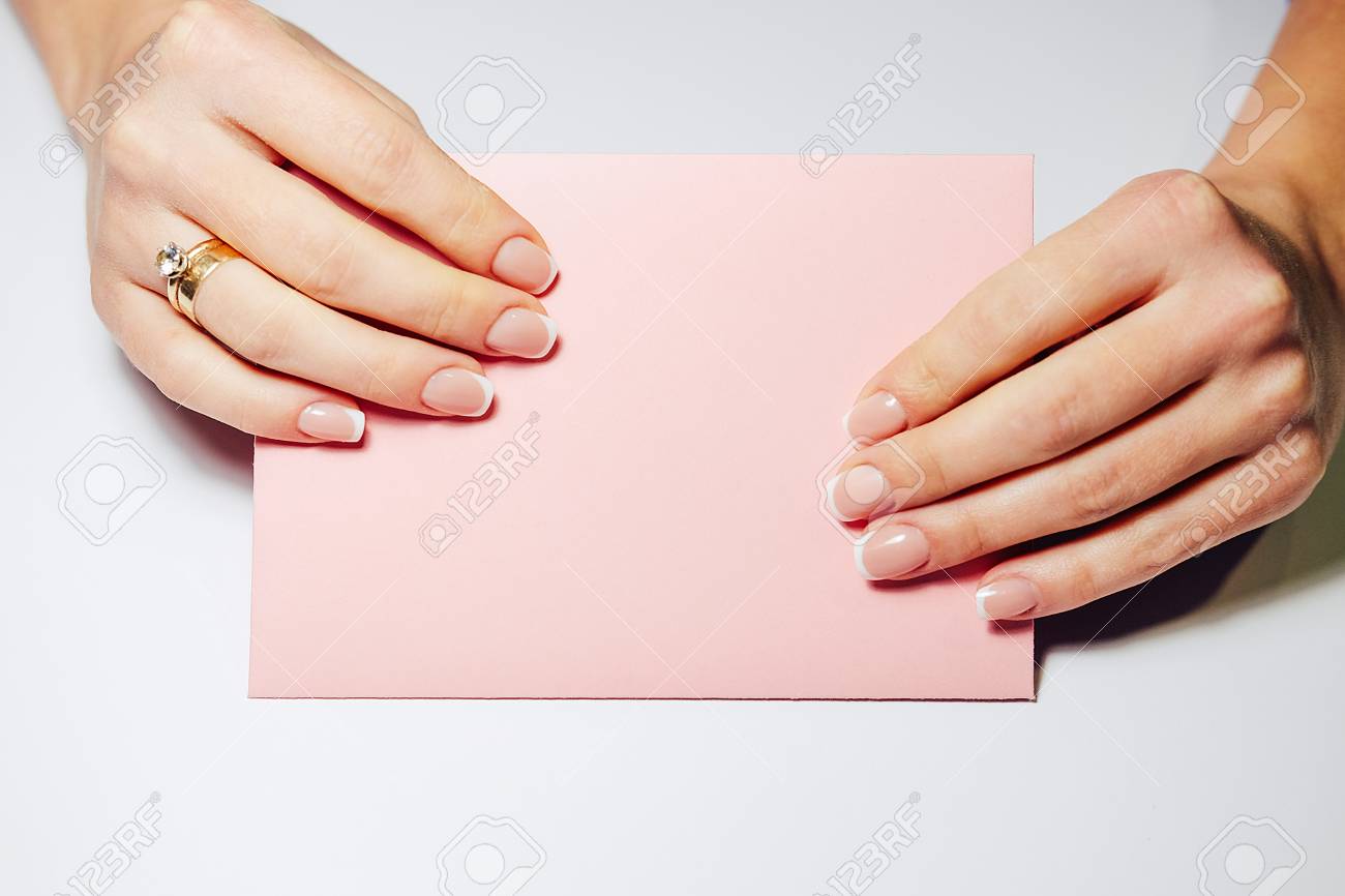 フランスの爪の延長 美しいマニキュアと結婚指輪を持つ女性は 結婚の招待状とピンクの封筒を保持しています の写真素材 画像素材 Image