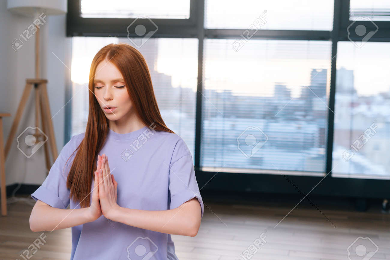 Close-up of redhead focused young woman meditating sitting on floor in lotus pose, Namaste mudra in light office room. Calm pretty redhead lady relaxation during yoga workout at home with closed eyes. - 169892794 Close-up of redhead focused young woman meditating sitting on floor in lotus pose, Namaste mudra in light office room. Calm pretty redhead lady relaxation during yoga workout at home with closed eyes. - 169892794