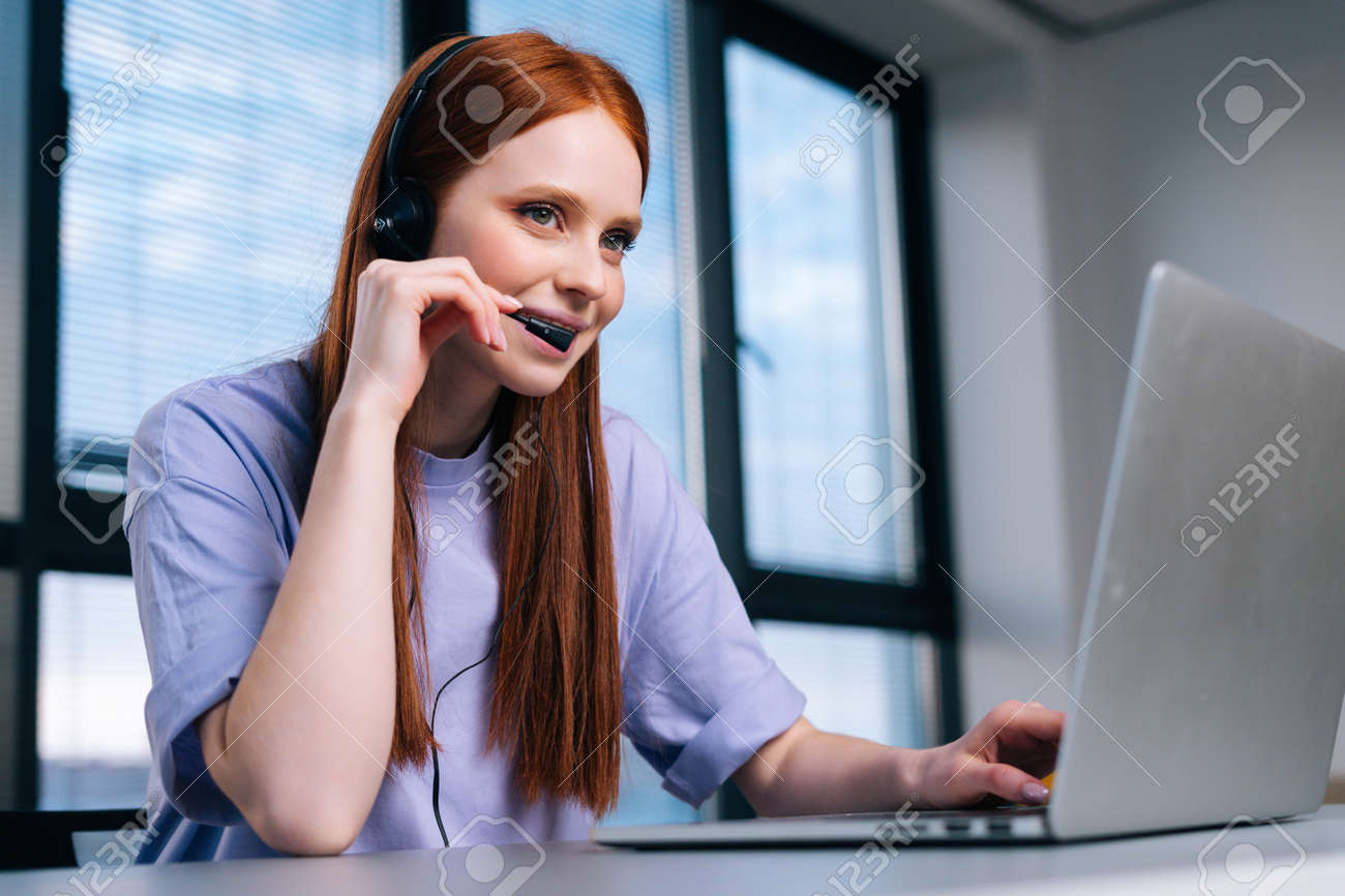 Close-up face of pretty young woman operator using headset and laptop during customer support at home office. Young female student communicating online by video call on background of window. - 169892891 Close-up face of pretty young woman operator using headset and laptop during customer support at home office. Young female student communicating online by video call on background of window. - 169892891