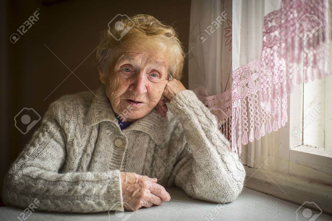 An elderly woman sits alone near the window. - 49489275 An elderly woman sits alone near the window. - 49489275