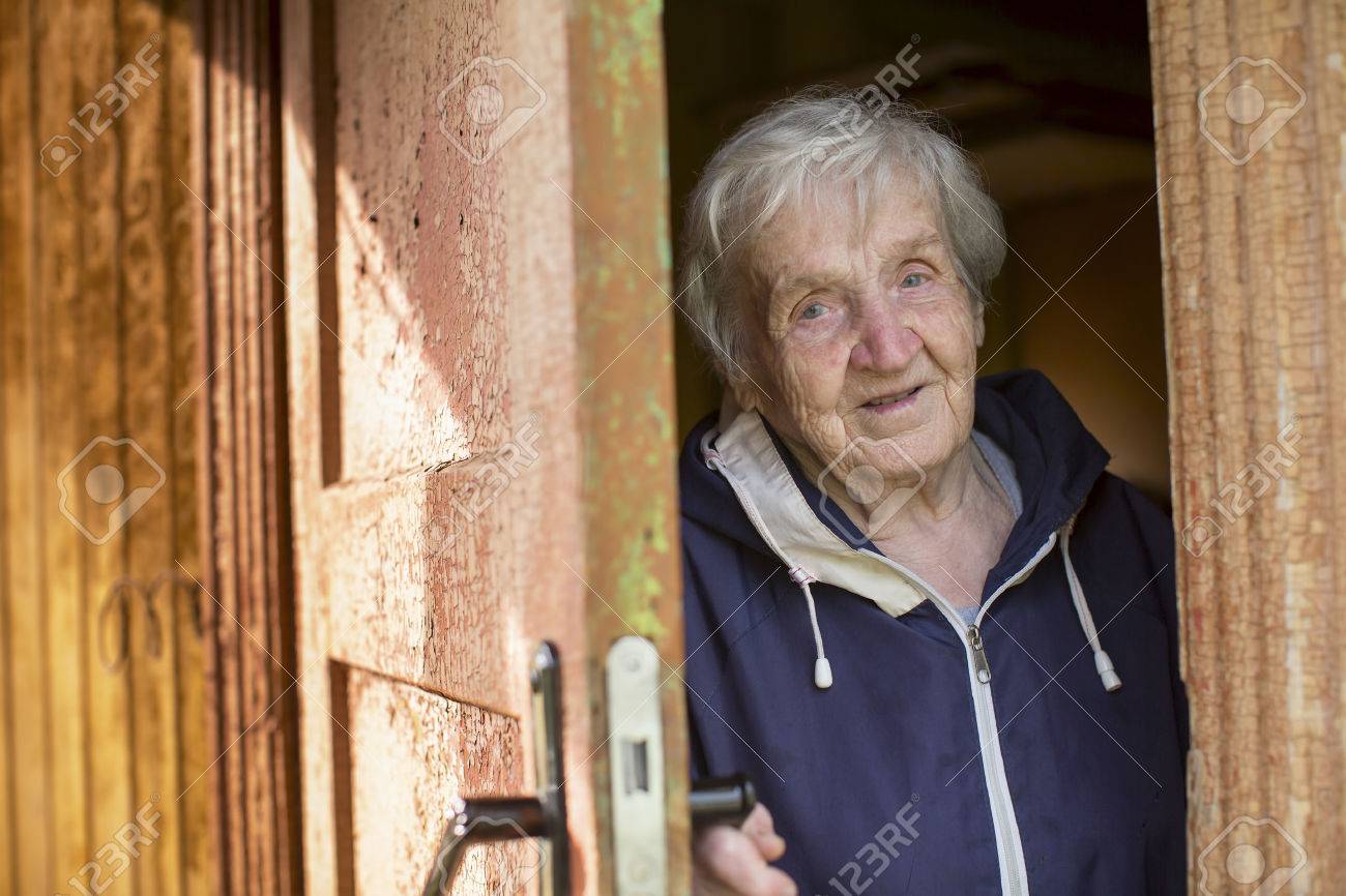 An elderly woman opens the door of the house. - 57102886 An elderly woman opens the door of the house. - 57102886