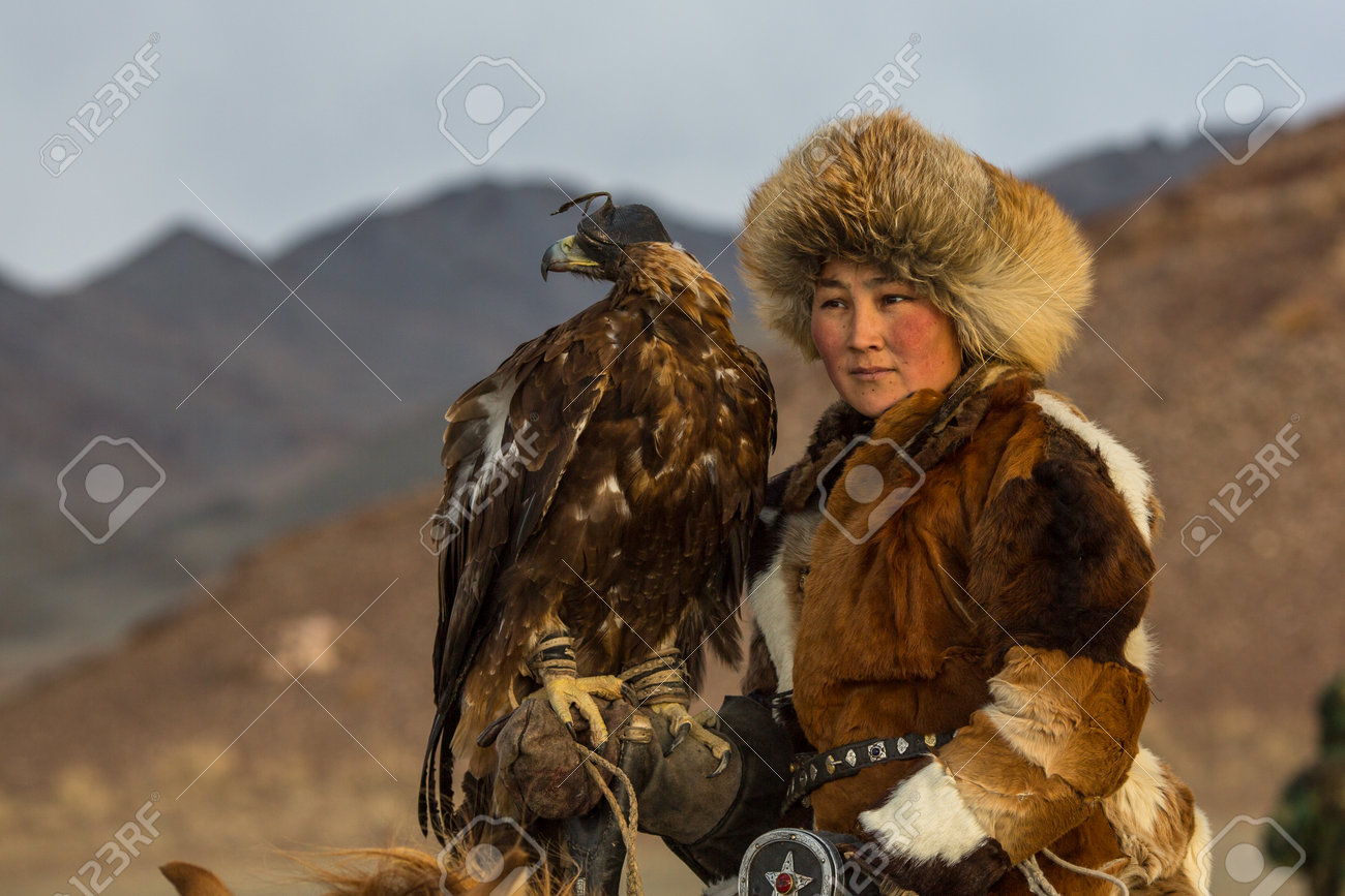 SAGSAY, MONGOLIA - SEP 28, 2017: Young woman Eagle Hunter at traditional clothing, while hunting to the hare holding a golden eagles on his arms in desert mountain of Western Mongolia. - 91157600 SAGSAY, MONGOLIA - SEP 28, 2017: Young woman Eagle Hunter at traditional clothing, while hunting to the hare holding a golden eagles on his arms in desert mountain of Western Mongolia. - 91157600