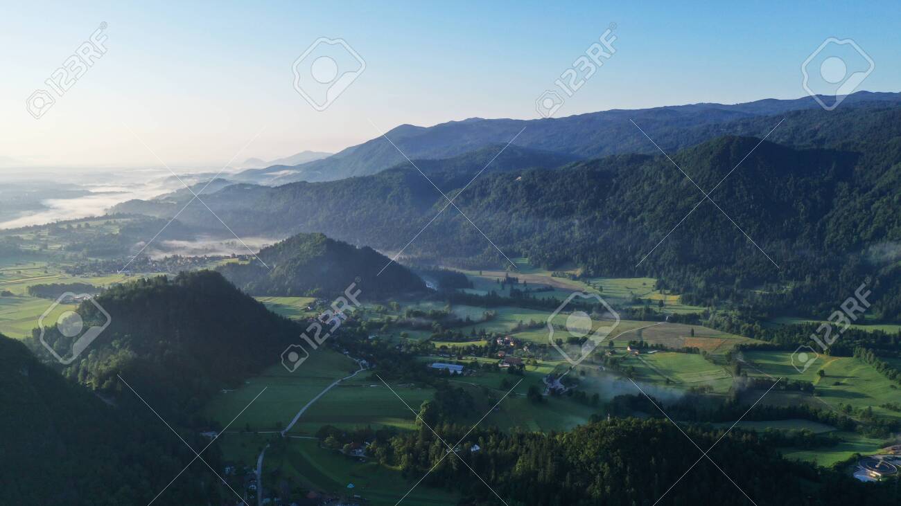 Aerial view of Bled Lake valley. Natural landscape with green meadows, fields, hills and mountains, small houses and trees. Sunny blue sky. Sun rays. - 141440845 Aerial view of Bled Lake valley. Natural landscape with green meadows, fields, hills and mountains, small houses and trees. Sunny blue sky. Sun rays. - 141440845