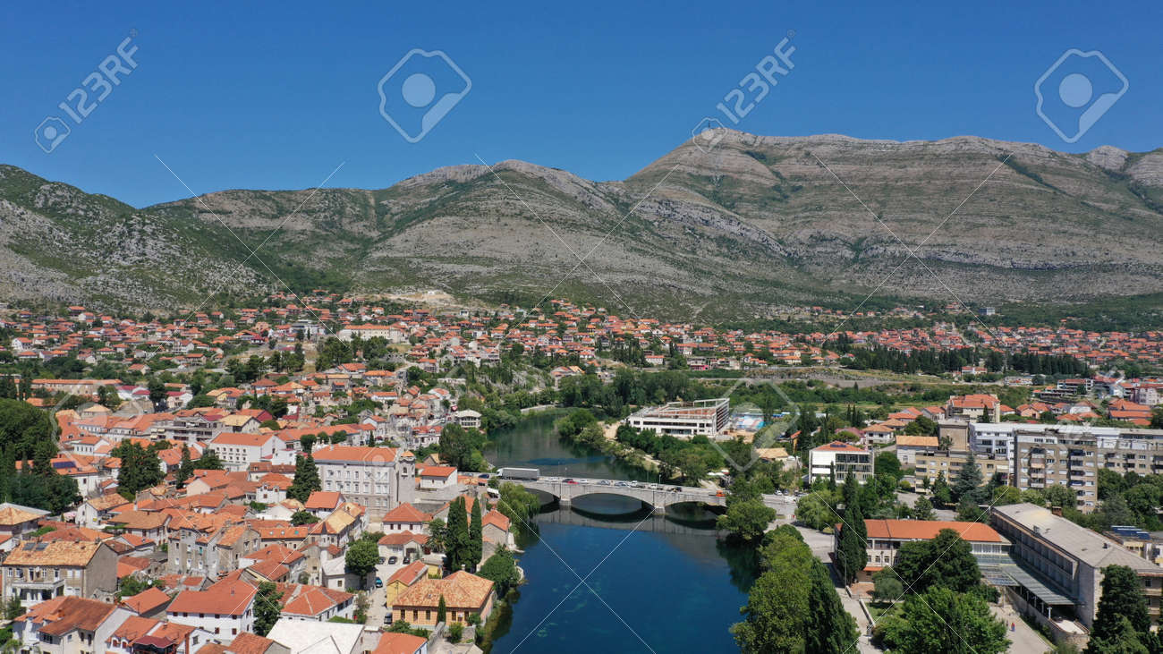 Aerial view of stone bridge (Kameni Most) on Trebisnjica river in Trebinje Old Town. Bosnia and Herzegovina. Summer sunny day, Turquoise water, mountains, trees, blue sky, small houses. - 139903402 Aerial view of stone bridge (Kameni Most) on Trebisnjica river in Trebinje Old Town. Bosnia and Herzegovina. Summer sunny day, Turquoise water, mountains, trees, blue sky, small houses. - 139903402