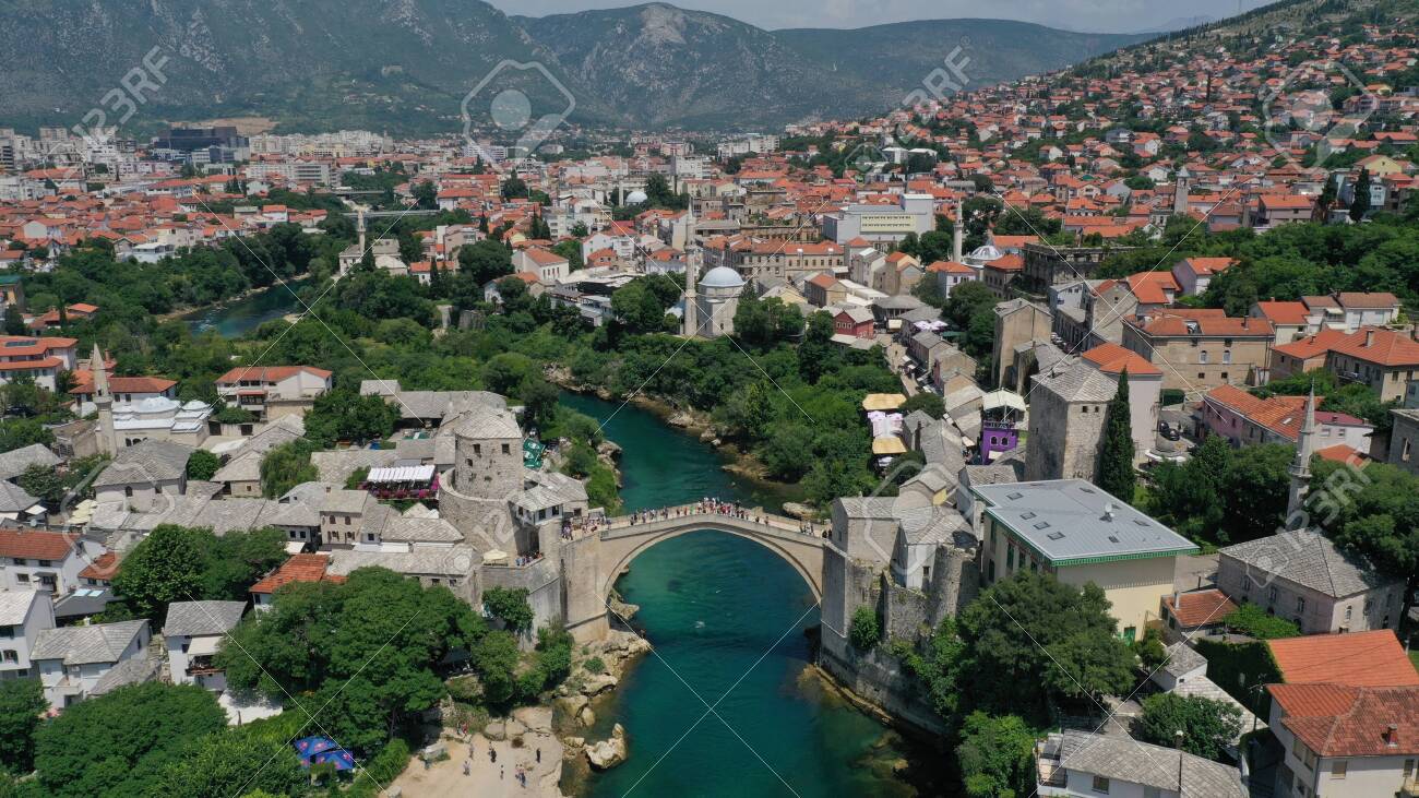 Aerial view of Stari Most old medieval bridge in Mostar, Neretva river, Bosnia and Herzegovina. Tourists walking on the bridge. Summer landscape of old town. Mosque on background. - 139967239 Aerial view of Stari Most old medieval bridge in Mostar, Neretva river, Bosnia and Herzegovina. Tourists walking on the bridge. Summer landscape of old town. Mosque on background. - 139967239