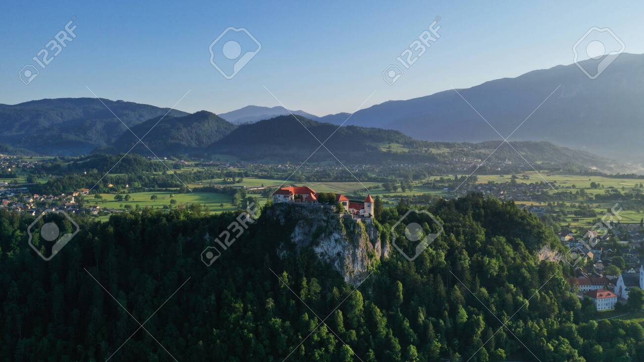Aerial footage of Bled castle on rocky cliff, Lake Bled in Slovenia, Europe. Natural mountainous landscape around castle, green meadows and fields. Summer. - 139967956 Aerial footage of Bled castle on rocky cliff, Lake Bled in Slovenia, Europe. Natural mountainous landscape around castle, green meadows and fields. Summer. - 139967956