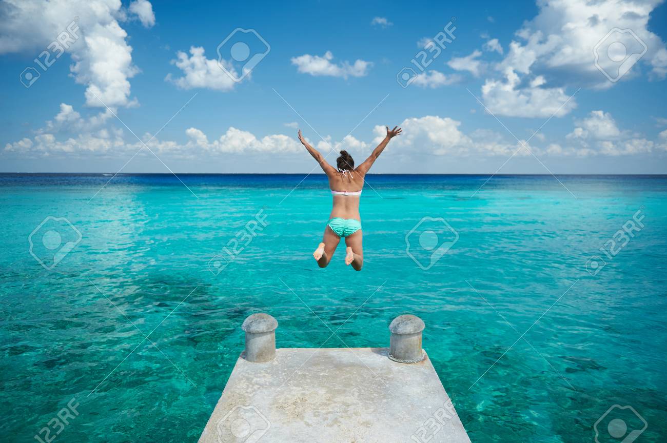 One woman jump in blue water from pier view from back on caribbean vacation - 70794146 One woman jump in blue water from pier view from back on caribbean vacation - 70794146
