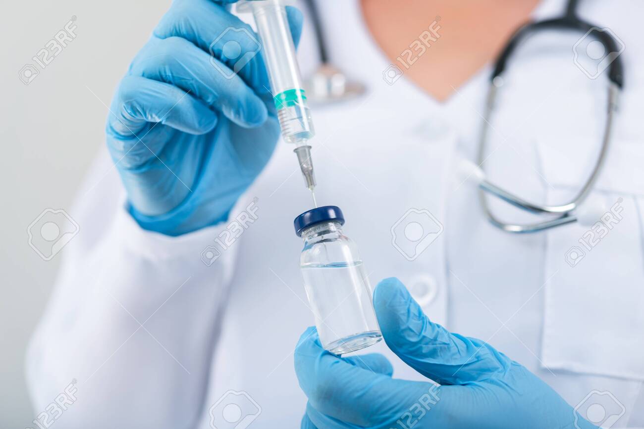 Female doctor holding flu vaccine in hands in clinic room. dose vaccination in hospital. - 129596637 Female doctor holding flu vaccine in hands in clinic room. dose vaccination in hospital. - 129596637