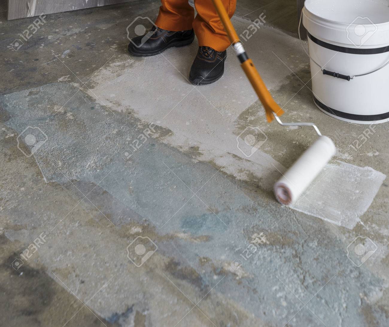 Worker Puts Primer With Roller On Concrete Floor Apartment Under