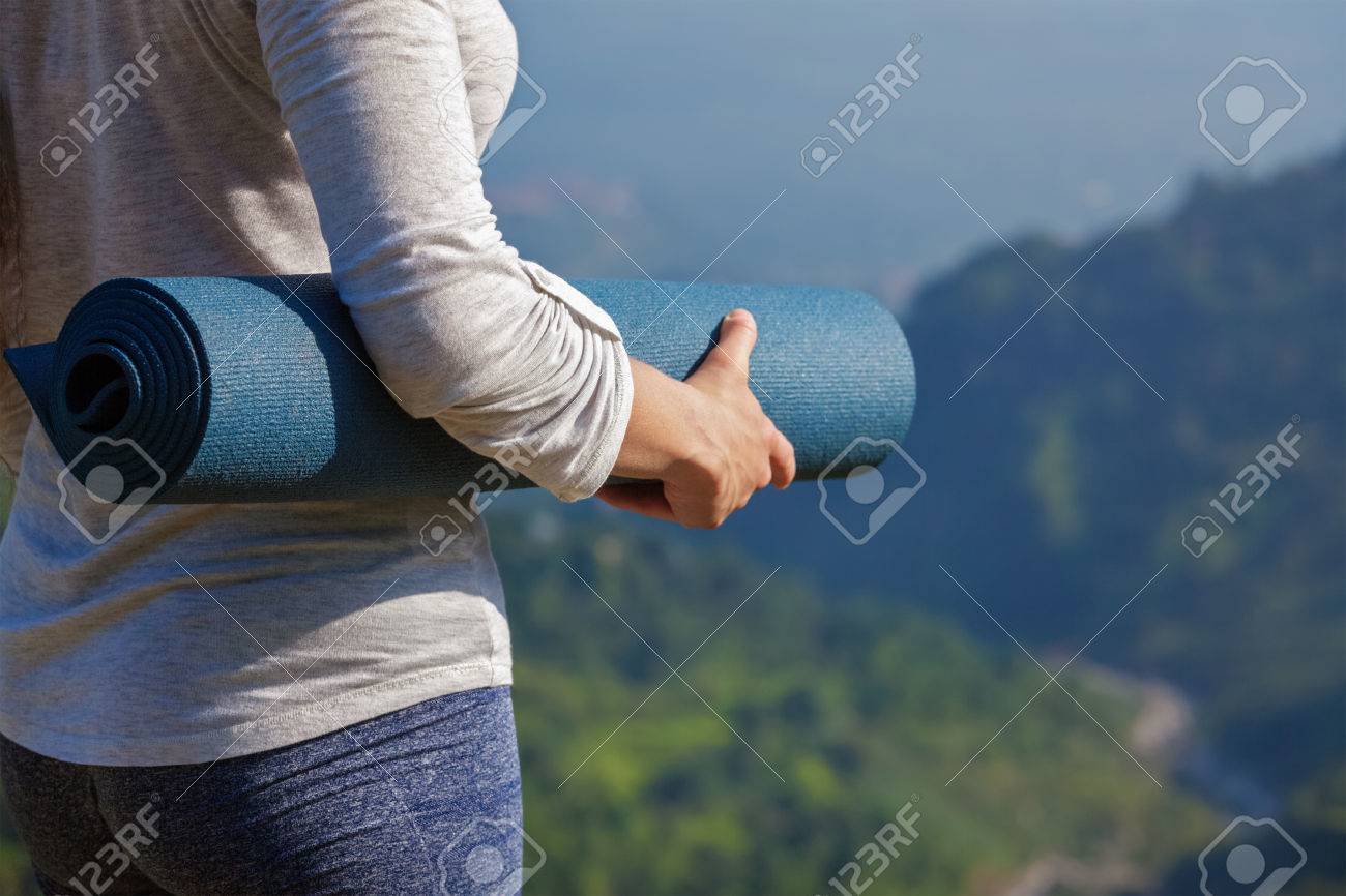 Woman standing with yoga mat outdoors in mountains close up with copyspace getting ready for yoga exercise - 63043170 Woman standing with yoga mat outdoors in mountains close up with copyspace getting ready for yoga exercise - 63043170
