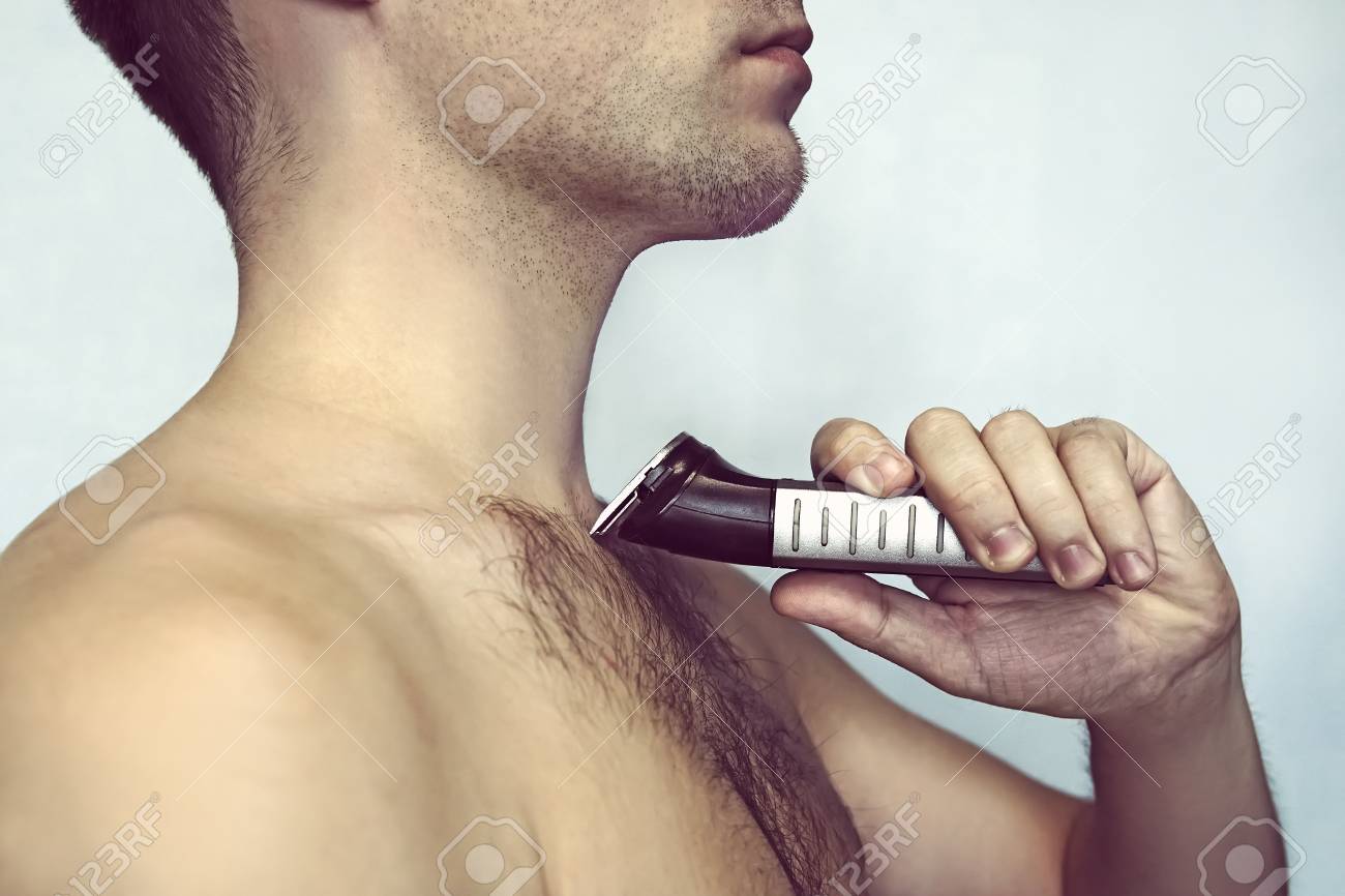 Handsome Young Bearded Man With A Trimmer Shaving Off Body Hair