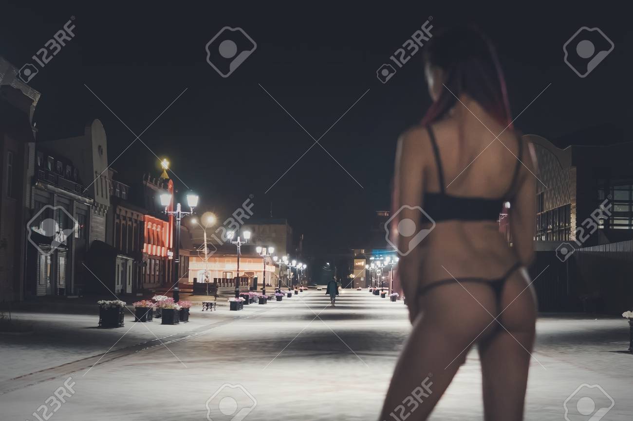 A half-naked woman stands on the street at night in the city..