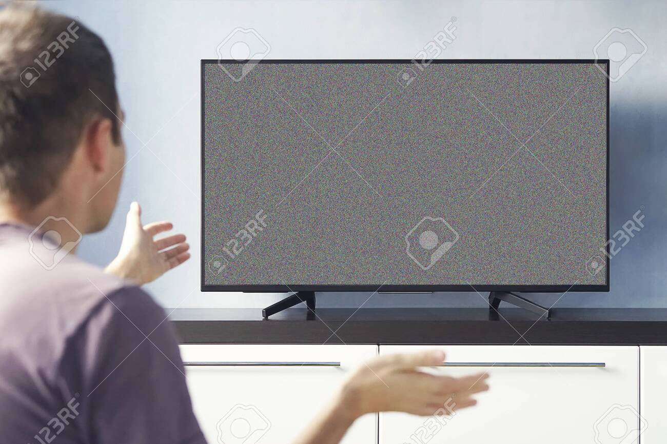 Frustrated Man Sitting On Sofa In Front Of Television With No Signal. young guy emotionally watching TV and waving his hands in discontent. - 138792021 Frustrated Man Sitting On Sofa In Front Of Television With No Signal. young guy emotionally watching TV and waving his hands in discontent. - 138792021