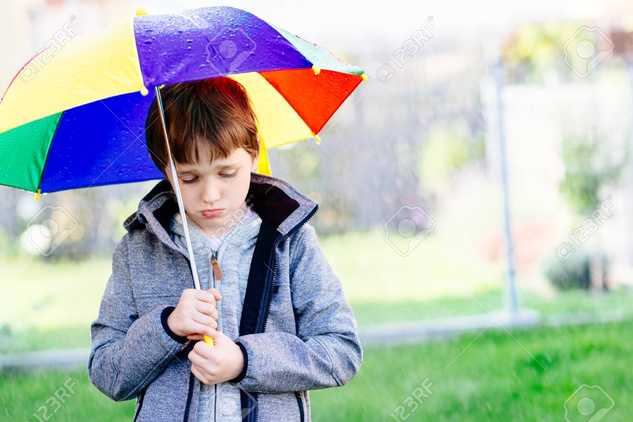 seven years old boy standing at the rain with colorful umbrella