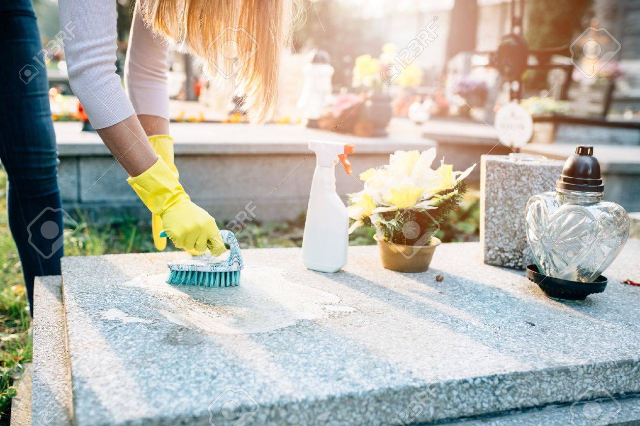 A woman cleans the grave. Washing tombstone with brush. Preparations for All Saints Day on November 1 - 63677640 A woman cleans the grave. Washing tombstone with brush. Preparations for All Saints Day on November 1 - 63677640
