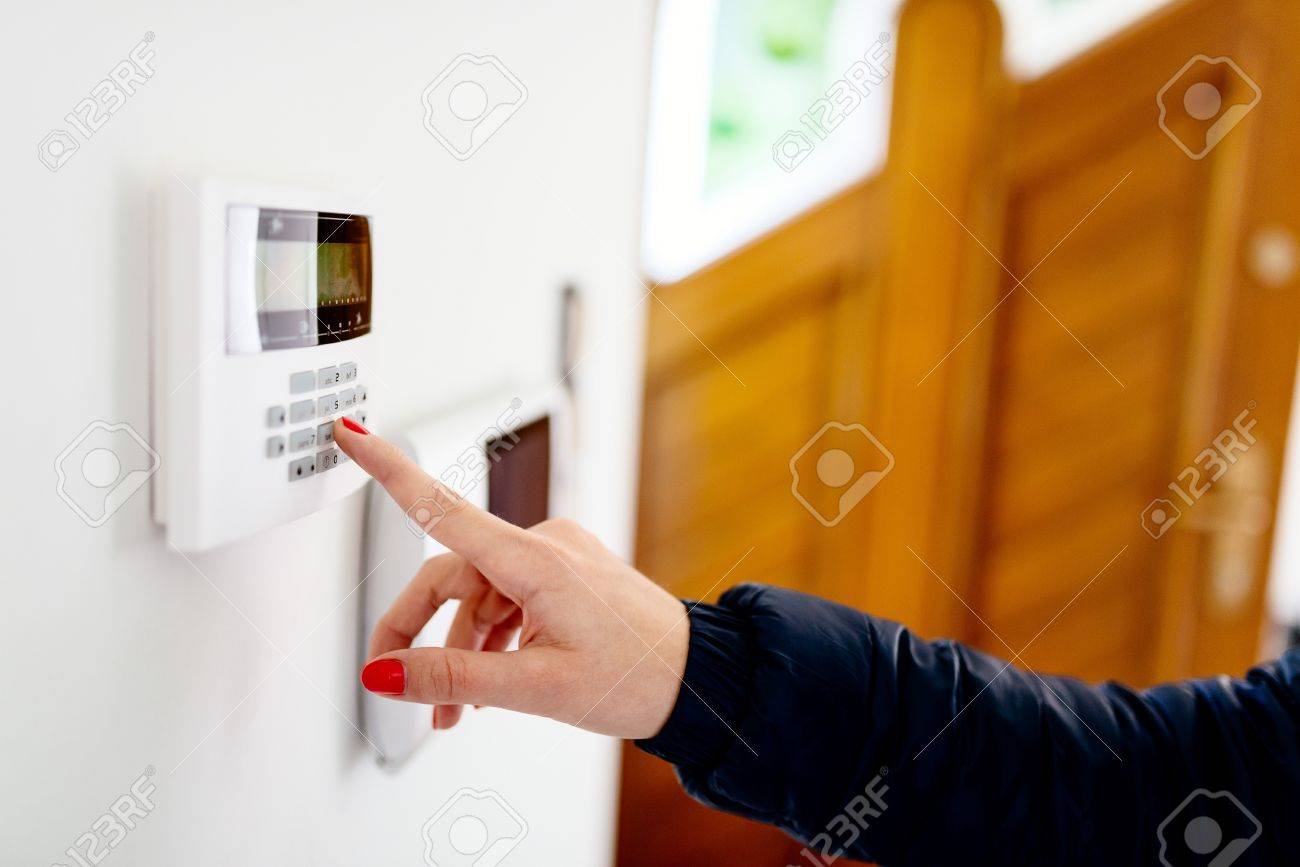 Young woman entering security code on home security alarm system keypad - 66755652 Young woman entering security code on home security alarm system keypad - 66755652