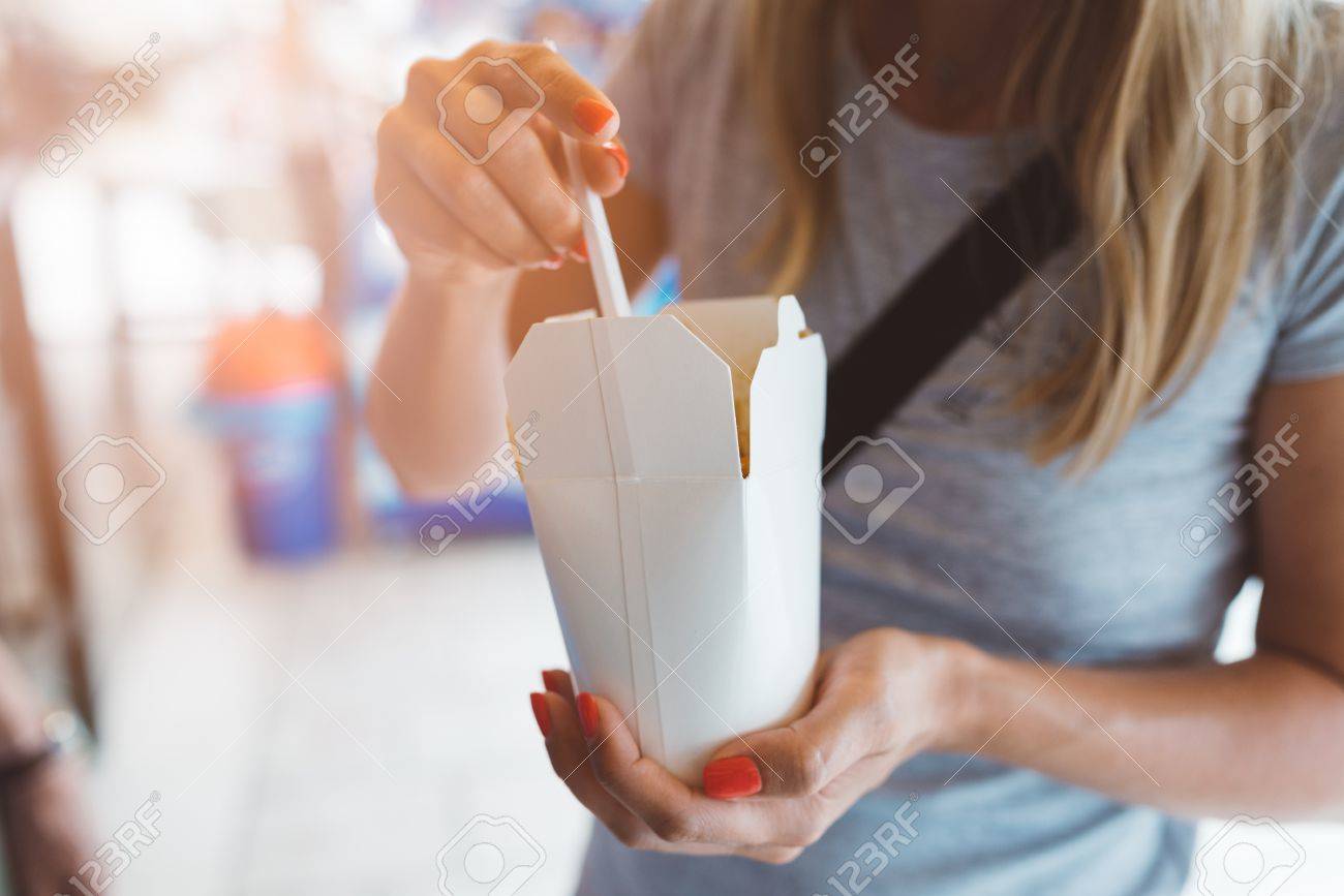 Woman eating fast food noodles from white carton box - 83777965 Woman eating fast food noodles from white carton box - 83777965