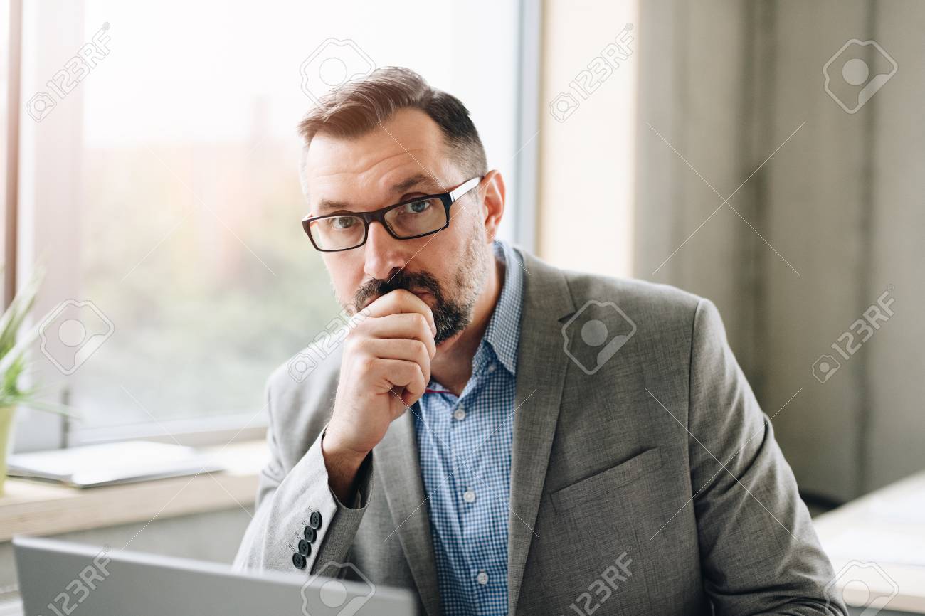 Thoughtful middle aged handsome businessman in shirt working on laptop computer in office. Man working in office - 116596243 Thoughtful middle aged handsome businessman in shirt working on laptop computer in office. Man working in office - 116596243