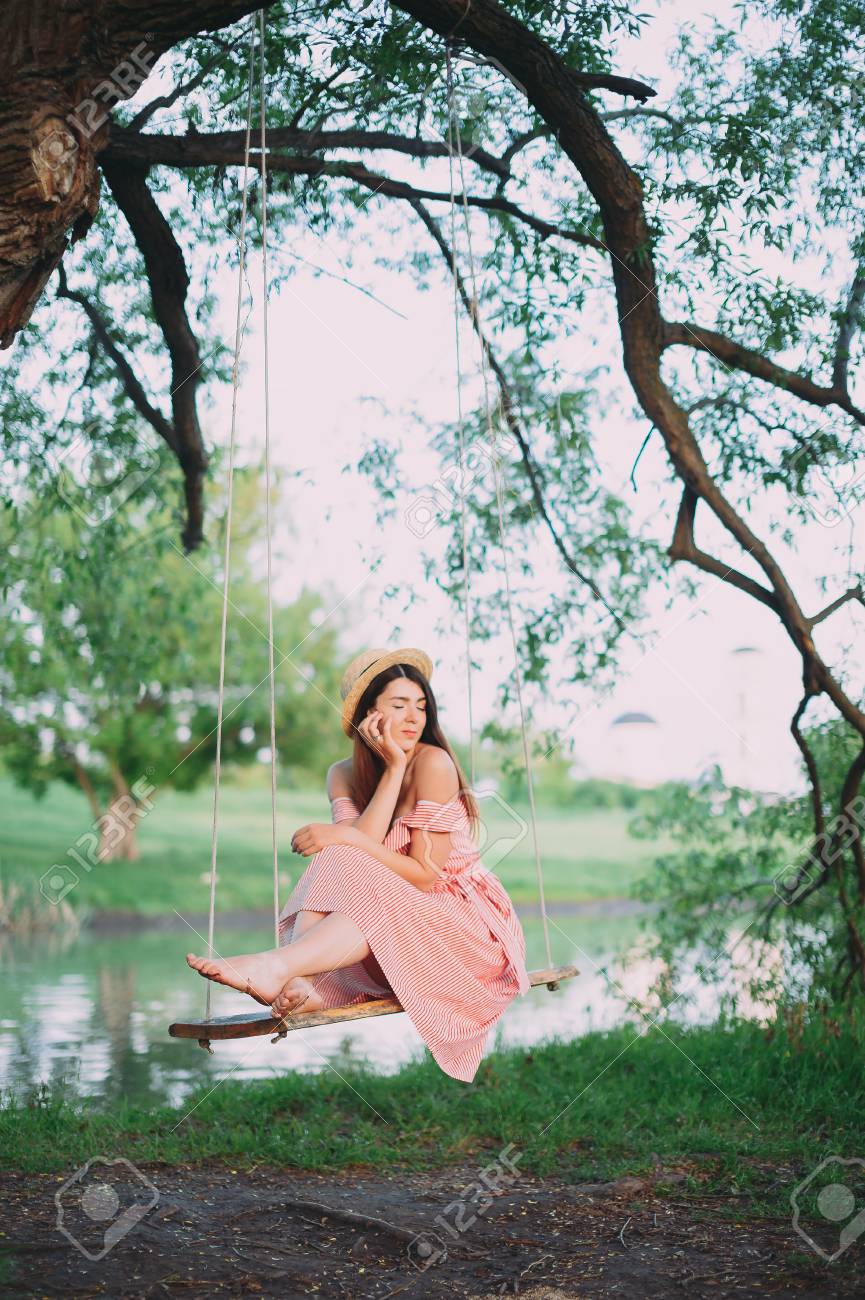 Beautiful Happy Girl In A Pink Dress Relaxes On A Swing Against Stock Photo Picture And Royalty Free Image Image