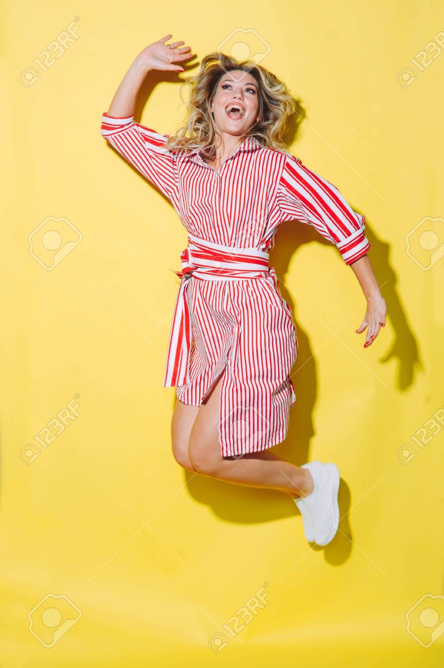 concept happy emotional young woman in red summer dress and hat jumping and laughing on yellow background - 147961494 concept happy emotional young woman in red summer dress and hat jumping and laughing on yellow background - 147961494