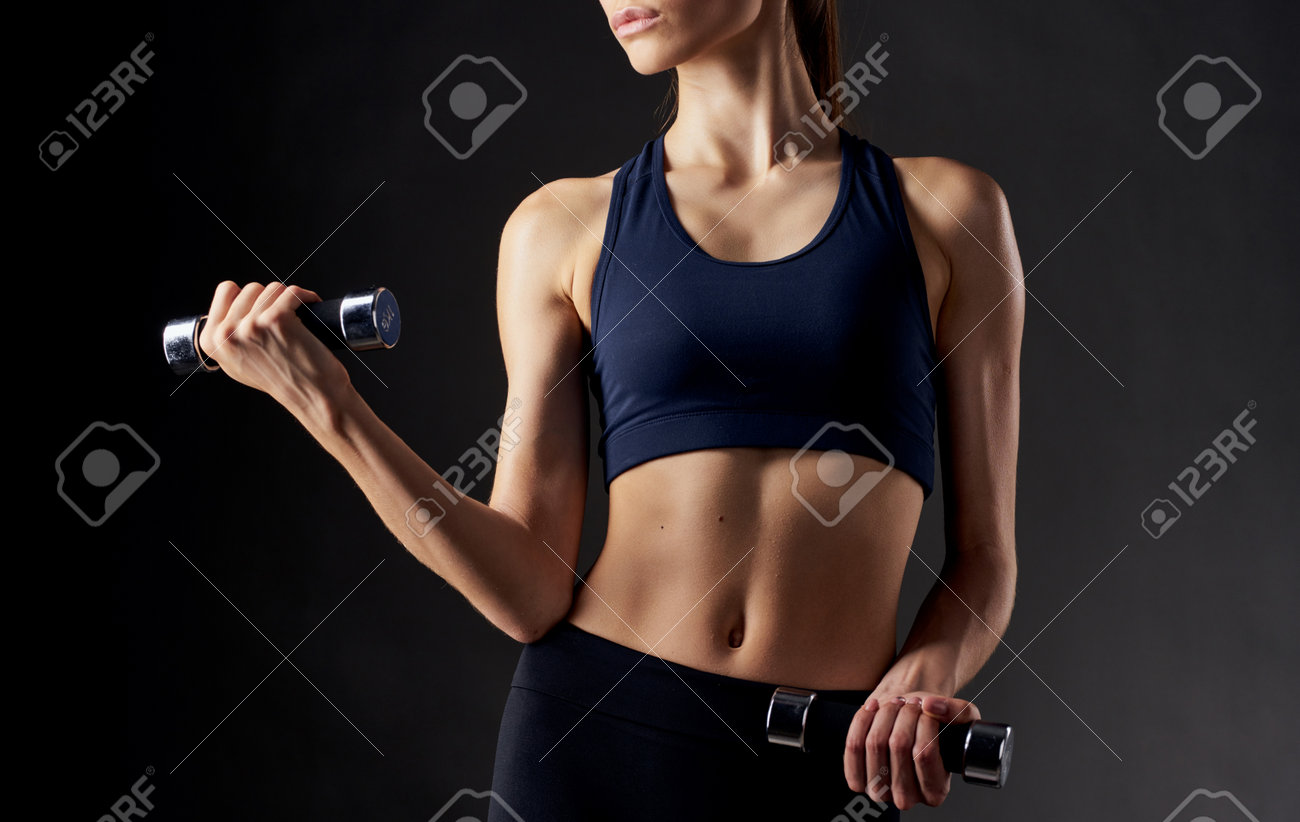 woman with pumped up abdominal muscles holds a dumbbell in her hand on a dark background - 165014774 woman with pumped up abdominal muscles holds a dumbbell in her hand on a dark background - 165014774