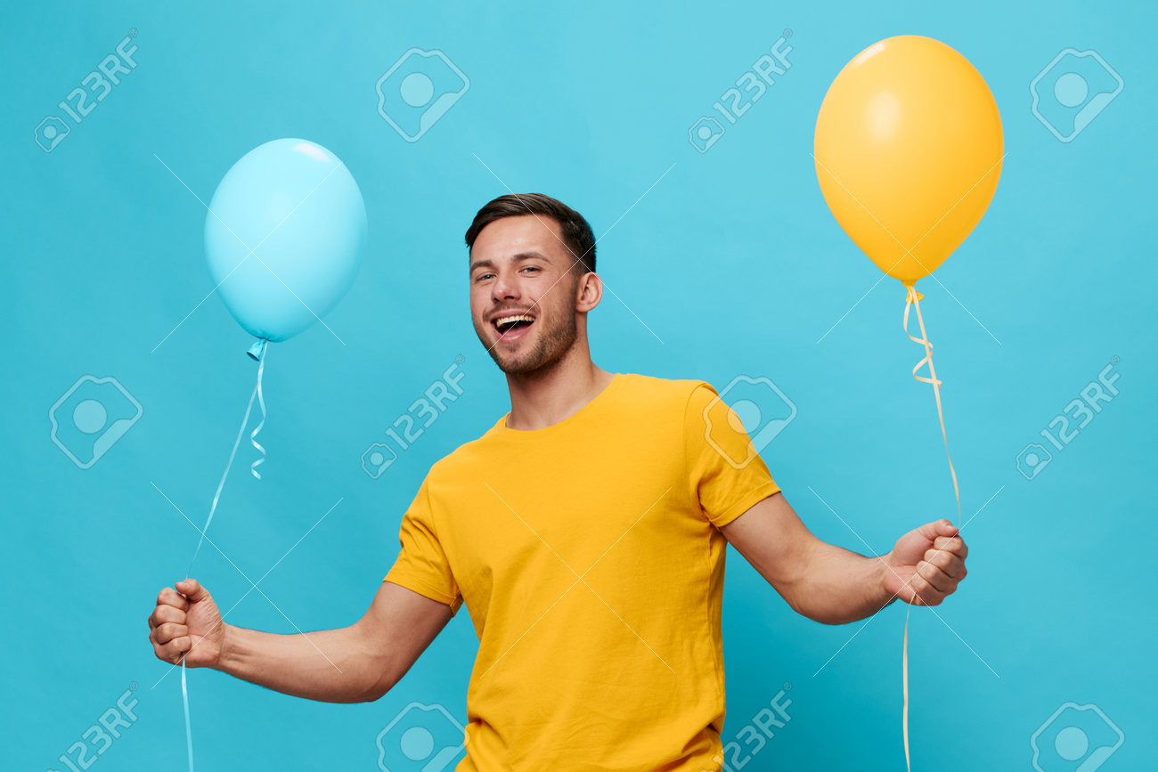 Cheerful Happy Friendly Tanned Handsome Man In Yellow T-shirt Smile At  Camera Hold Balloons Posing Isolated On Blue Studio Background. Copy Space  Banner Mockup. Friendship Concept Stock Photo, Picture and Royalty Free, image size:1300x867