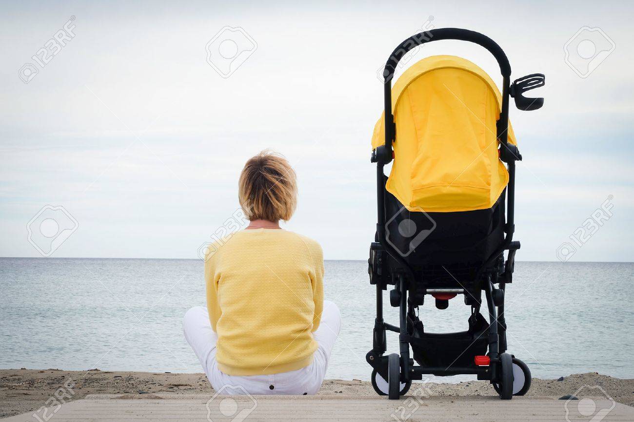 Woman looking through the sea while sitting on beach with baby carriage. Young mother sitting outdoor with stroller. Maternity concept with copyspace - 71856557 Woman looking through the sea while sitting on beach with baby carriage. Young mother sitting outdoor with stroller. Maternity concept with copyspace - 71856557