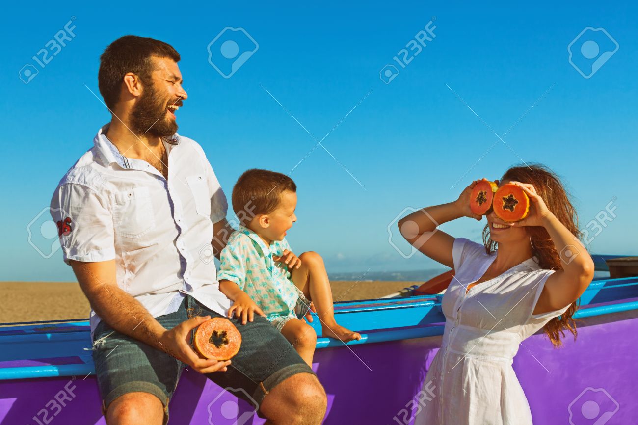 幸せな面白い家族 父 母 赤ちゃんの息子は 海砂のビーチで一緒に歩きます 人々 があるピクニック 楽しいトロピカル フルーツのパパイヤを食べる 旅行 アクティブなライフ スタイル 夏の休日に子供を持つ親です の写真素材 画像素材 Image